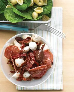 Martha Stewart antipasto salad with pepperoni, bocconcini, olives and sun-dried tomatoes in a white bowl beside pasta shells and spinach