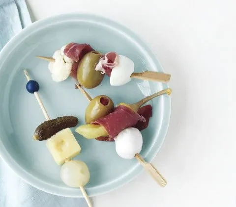 Martha Stewart antipasto skewers with green olives, prosciutto, mozzarella and giardiniera on a pale blue plate