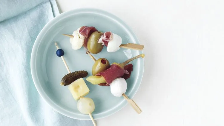 Martha Stewart antipasto skewers with green olives, prosciutto, mozzarella and giardiniera on a pale blue plate