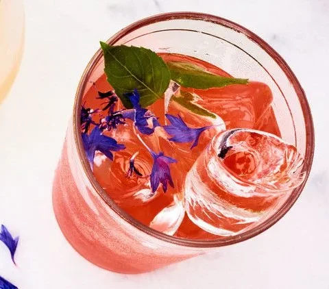 Martha Stewart Aperol gin punch in a glass with ice, a basil sprig and blue cornflower petals