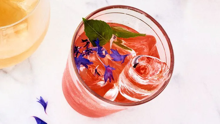 Martha Stewart Aperol gin punch in a glass with ice, a basil sprig and blue cornflower petals