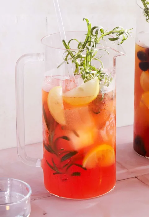 Martha Stewart Aperol Jasmine Spritz in a glass pitcher with lemon wedges, ice and rosemary sprigs