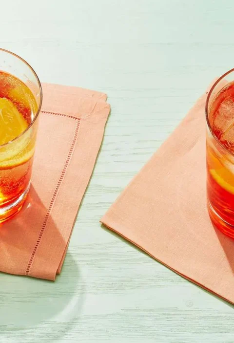 Two Martha Stewart Aperol Spritz drinks with ice and orange slices in glasses on peach napkins