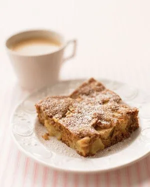 Martha Stewart apple cake square dusted with confectioners' sugar on a white plate next to a cup of coffee