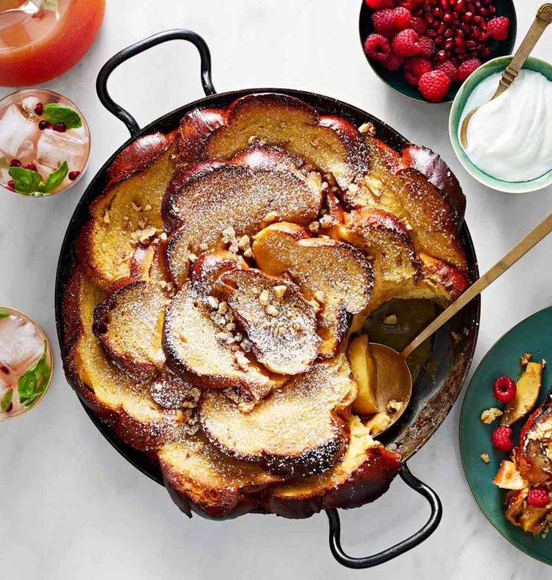 Martha Stewart apple-caramel French toast baked in a black skillet with shingled challah, dusted with confectioners' sugar and chopped pecans