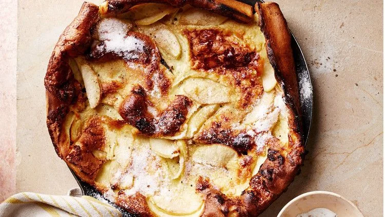 Martha Stewart apple-cardamom brown-butter Dutch baby, puffed and golden in a skillet with apple slices and powdered sugar on top