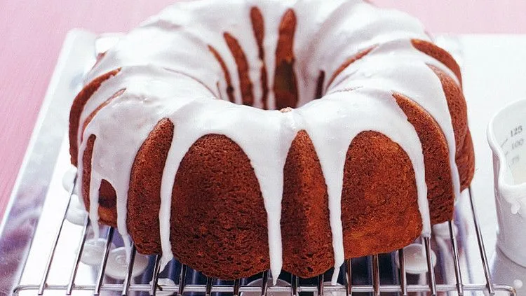 Martha Stewart apple-cinnamon Bundt cake with white glaze dripping down the sides on a wire cooling rack