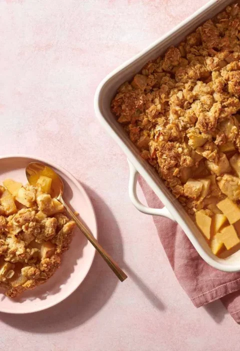 Martha Stewart apple crisp with golden oat topping in a white baking dish next to a plated serving