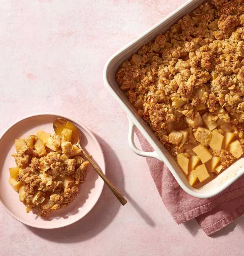 Martha Stewart apple crisp with golden oat topping in a white baking dish next to a plated serving