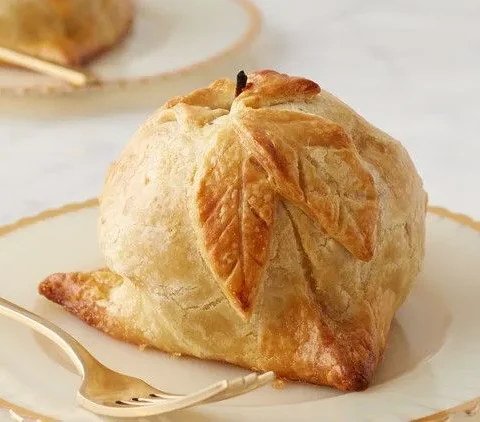Martha Stewart apple dumplings with a golden pastry leaf design and exposed apple stem on a gold-rimmed plate