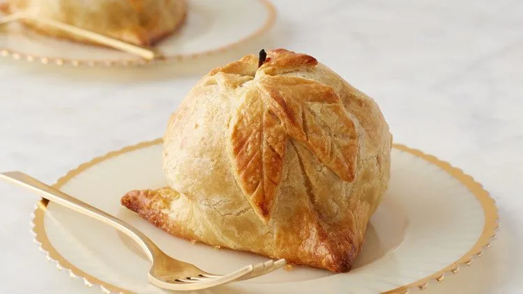 Martha Stewart apple dumplings with a golden pastry leaf design and exposed apple stem on a gold-rimmed plate