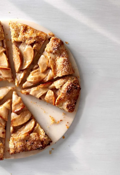 Martha Stewart apple galette with golden folded crust and sliced apple wedges, cut into pieces on a round board