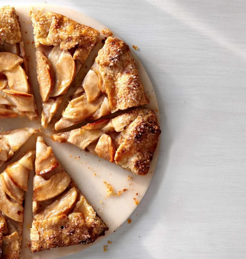 Martha Stewart apple galette with golden folded crust and sliced apple wedges, cut into pieces on a round board
