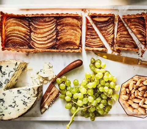 Martha Stewart apple-membrillo tart with shingled apple slices, sliced on a board with blue cheese, green grapes and Marcona almonds