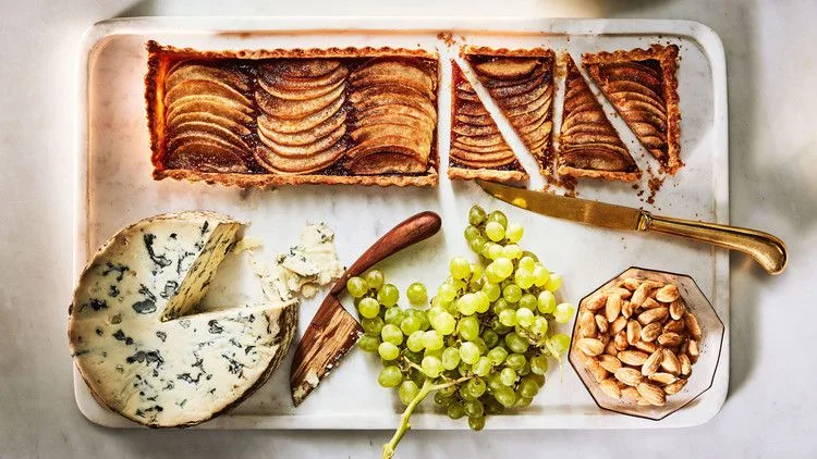 Martha Stewart apple-membrillo tart with shingled apple slices, sliced on a board with blue cheese, green grapes and Marcona almonds