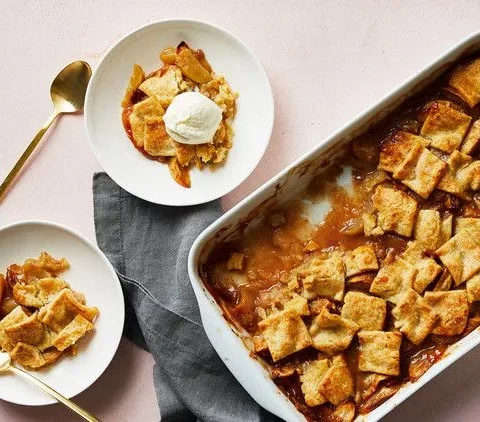 Martha Stewart apple pandowdy in a white baking dish topped with golden pastry squares, with two plates and a scoop of vanilla ice cream beside it