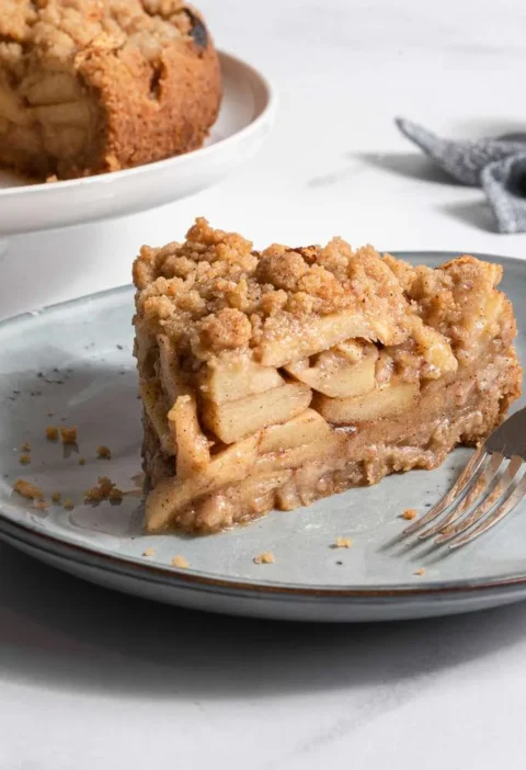 Slice of Martha Stewart apple-pie cake with a crumb topping and layered apples on a gray plate with a fork