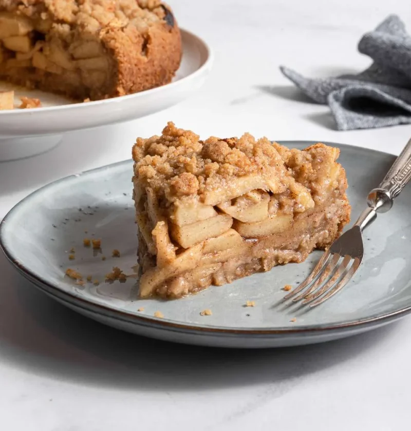 Slice of Martha Stewart apple-pie cake with a crumb topping and layered apples on a gray plate with a fork
