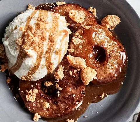 Martha Stewart apple sundaes with cider caramel sauce, baked apple rounds topped with vanilla ice cream, caramel and crushed cookies in a gray bowl