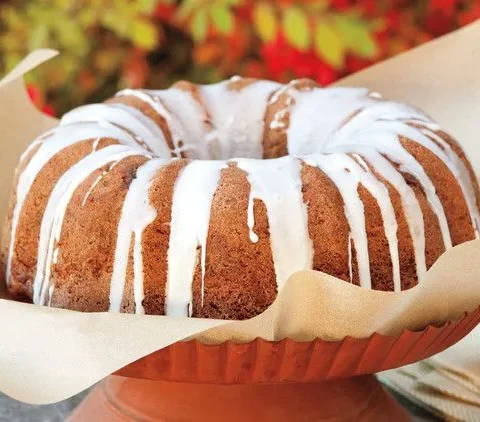 Martha Stewart apple-walnut Bundt cake with white apple cider glaze dripping down the sides, served on parchment on a terracotta cake stand
