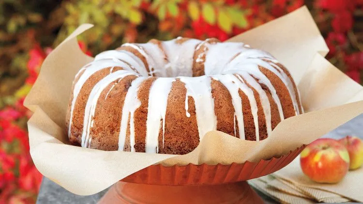 Martha Stewart apple-walnut Bundt cake with white apple cider glaze dripping down the sides, served on parchment on a terracotta cake stand