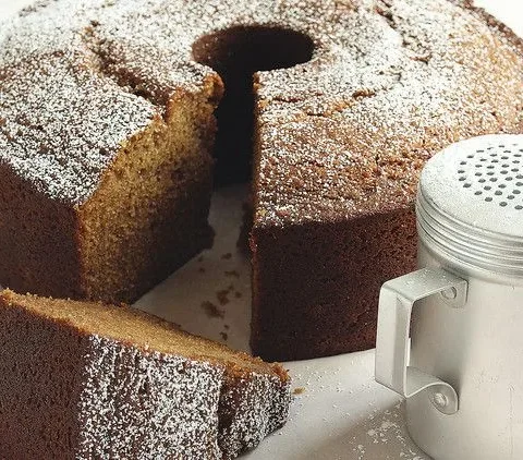 Martha Stewart applesauce cake dusted with confectioners' sugar on a board with a slice cut and a sugar shaker beside it