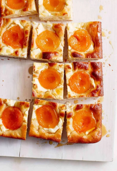 Martha Stewart apricot-and-cream cheese squares with golden crust, apricot halves and honey drizzle on a wooden board