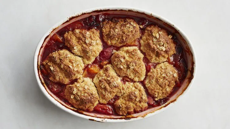Martha Stewart apricot cobbler in an oval baking dish with golden oat-topped biscuits over bubbling red fruit