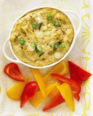Martha Stewart artichoke dip in a white baking dish topped with sliced scallions next to red and yellow pepper wedges