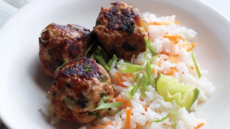 Martha Stewart Asian turkey meatballs with carrot rice, scallions and a lime wedge on a white plate