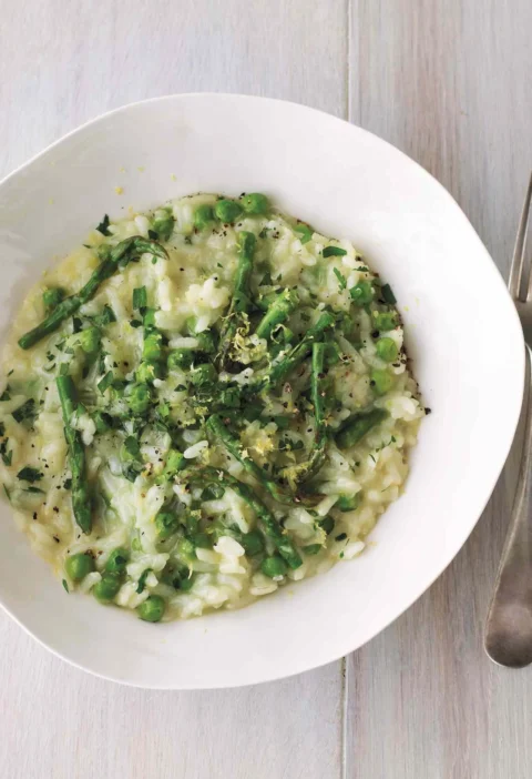 Martha Stewart asparagus-and-lemon risotto with green peas, asparagus pieces and lemon zest in a white bowl beside a fork