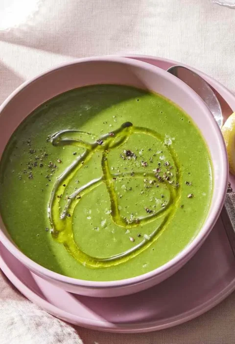 Martha Stewart asparagus and potato soup with ginger in a pink bowl, drizzled with olive oil and black pepper beside lemon wedges