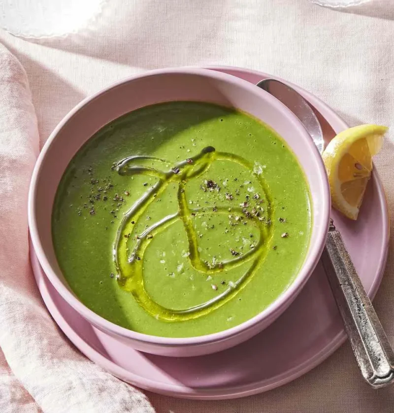 Martha Stewart asparagus and potato soup with ginger in a pink bowl, drizzled with olive oil and black pepper beside lemon wedges