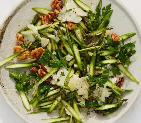 Martha Stewart asparagus and walnut salad with thin asparagus slices, toasted walnuts, parsley and shaved Pecorino on a round plate