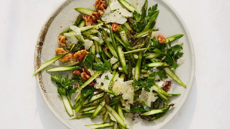 Martha Stewart asparagus and walnut salad with thin asparagus slices, toasted walnuts, parsley and shaved Pecorino on a round plate
