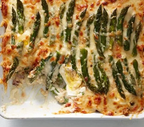 Martha Stewart asparagus casserole in a white baking dish topped with golden melted gruyere and asparagus spears