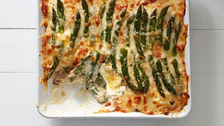 Martha Stewart asparagus casserole in a white baking dish topped with golden melted gruyere and asparagus spears