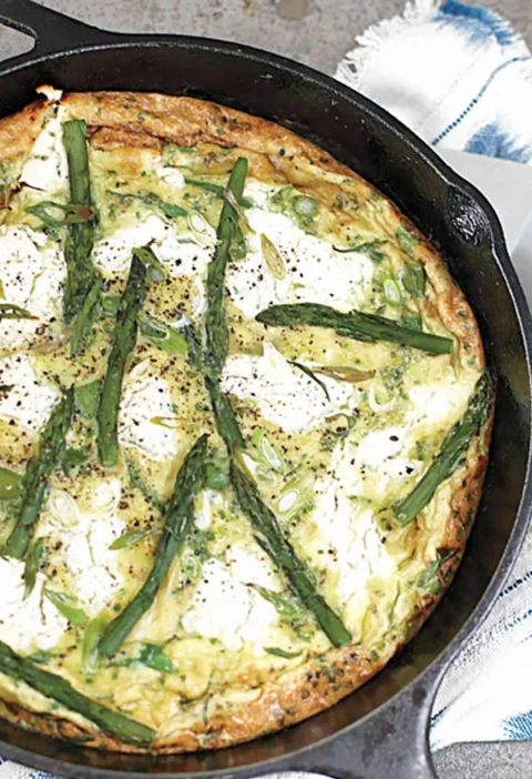 Martha Stewart asparagus frittata with goat cheese and herbs in a cast iron skillet topped with whole asparagus spears