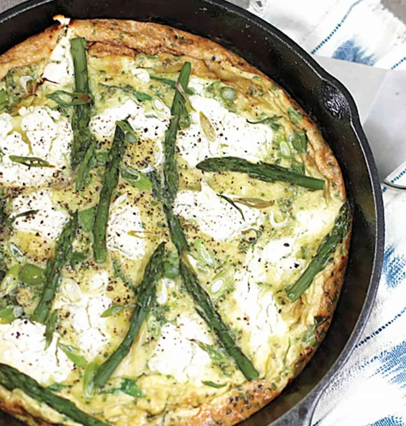 Martha Stewart asparagus frittata with goat cheese and herbs in a cast iron skillet topped with whole asparagus spears