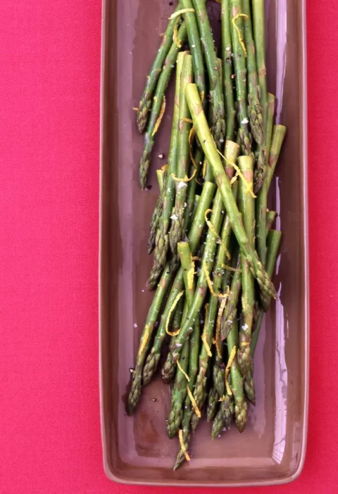 Martha Stewart asparagus with lemon butter, tender green spears with lemon zest and salt on a long brown dish