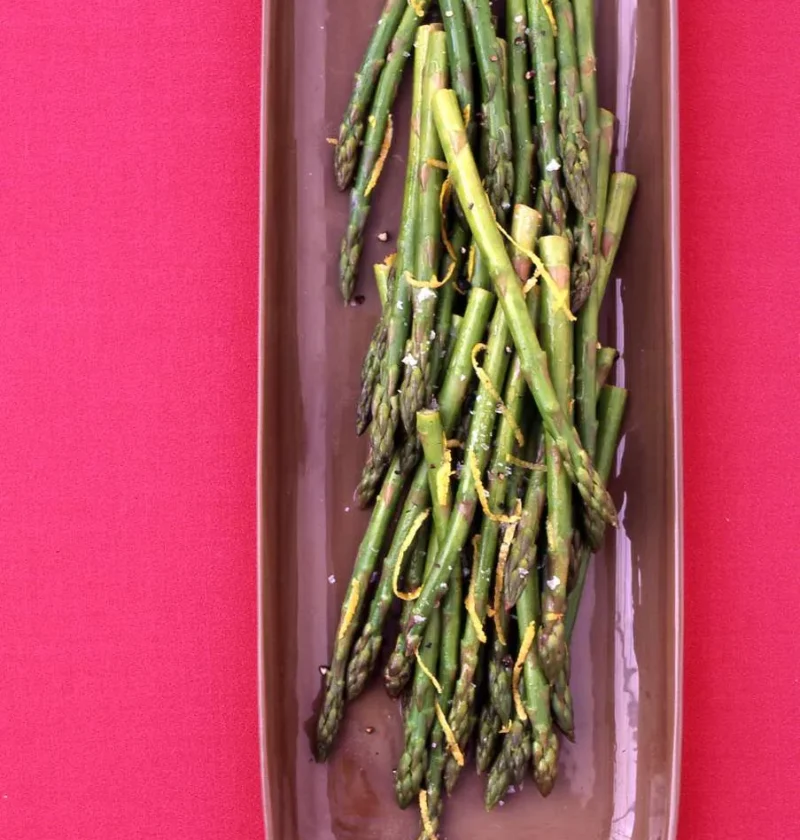 Martha Stewart asparagus with lemon butter, tender green spears with lemon zest and salt on a long brown dish
