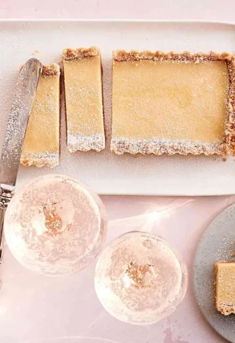 Martha Stewart Atlantic-Beach-Tart bars with a saltine crust and lemon filling dusted with confectioners' sugar on a white platter with coupe glasses
