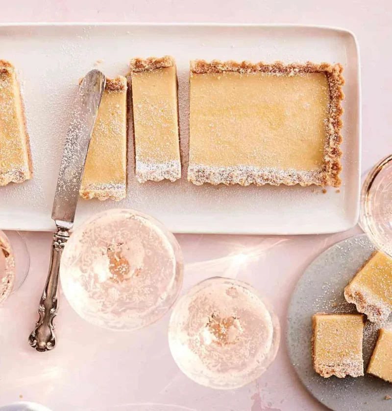 Martha Stewart Atlantic-Beach-Tart bars with a saltine crust and lemon filling dusted with confectioners' sugar on a white platter with coupe glasses