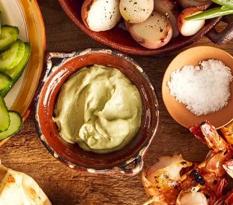 Martha Stewart avocado cream sauce in a rustic clay bowl next to grilled shrimp, cucumber slices, potatoes and green beans