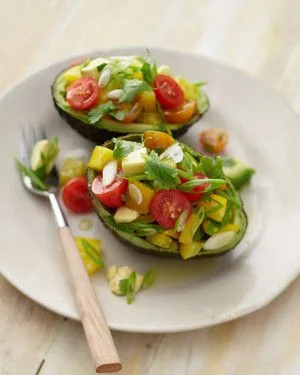 Martha Stewart avocado with bell pepper and tomatoes, two avocado halves filled with diced yellow pepper, cherry tomatoes and cilantro on a white plate