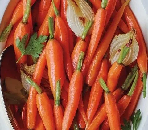 Martha Stewart baby carrots with spring onions glazed in butter and served in a white oval dish with parsley leaves