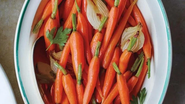 Martha Stewart baby carrots with spring onions glazed in butter and served in a white oval dish with parsley leaves