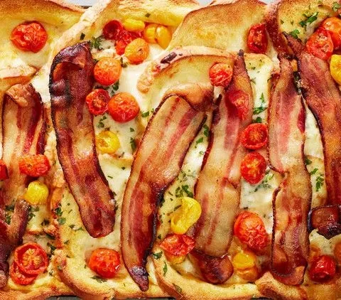 Martha Stewart bacon, egg, and cheese baked French toast topped with bacon strips and roasted cherry tomatoes on a sheet pan