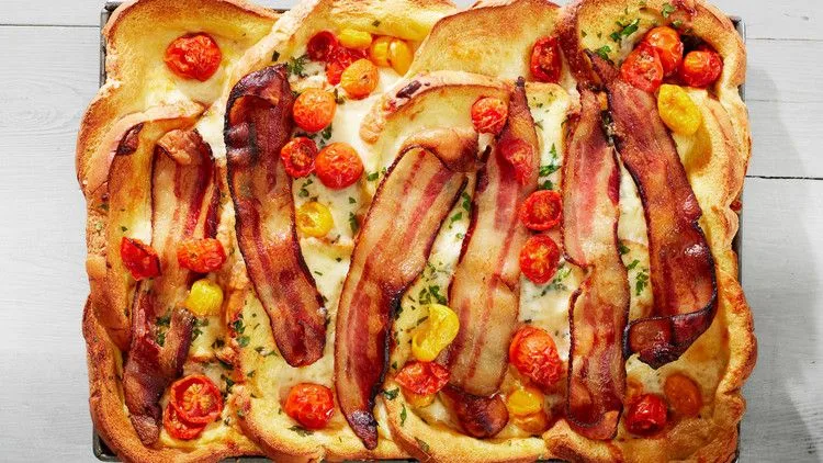 Martha Stewart bacon, egg, and cheese baked French toast topped with bacon strips and roasted cherry tomatoes on a sheet pan