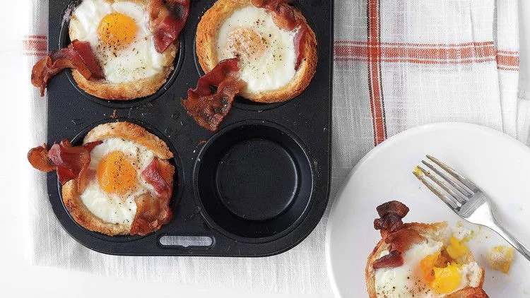 Martha Stewart bacon, egg and toast cups in a muffin tin with bacon slices and baked eggs, plus one served on a white plate with a fork